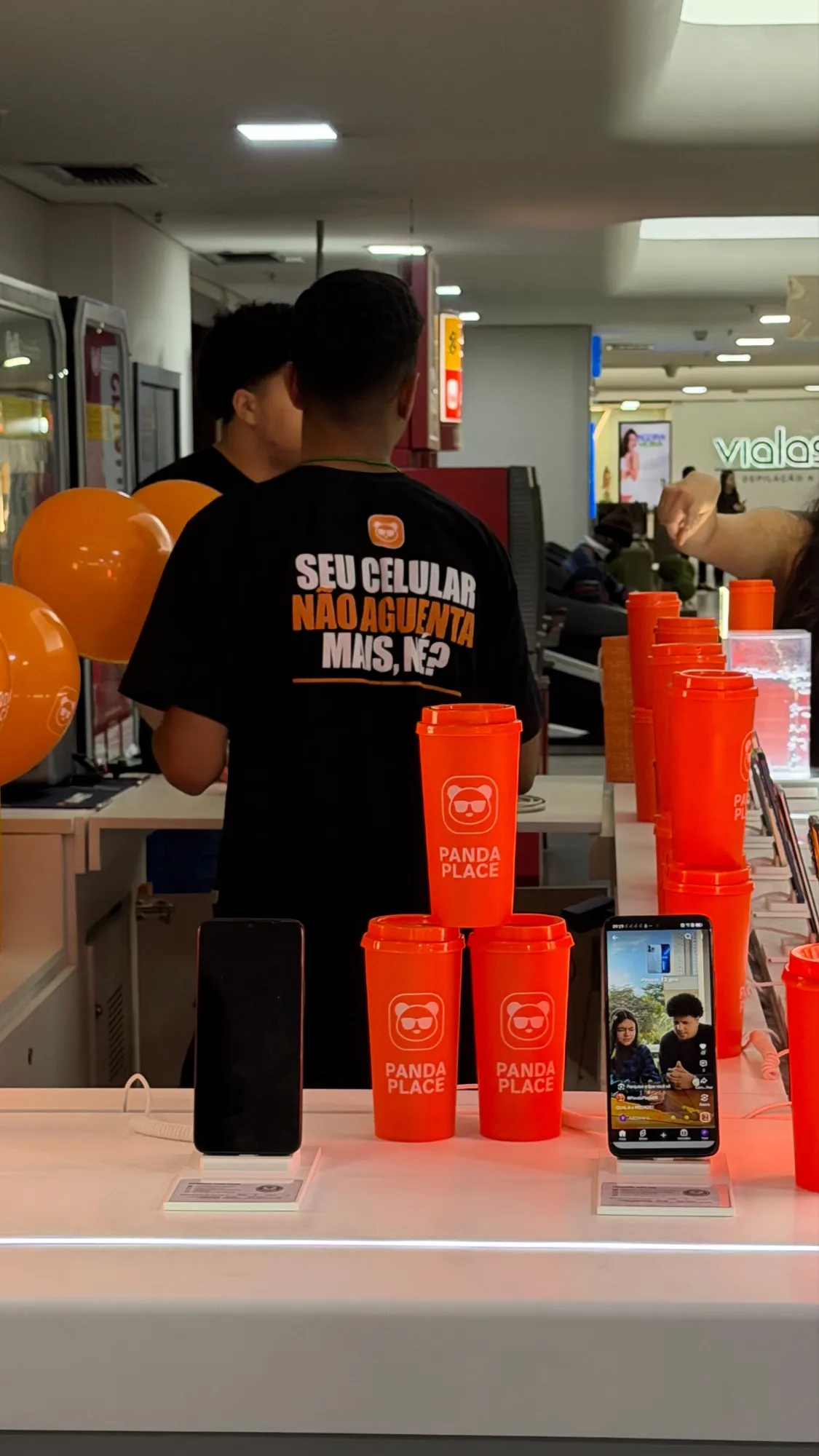 Equipe Panda Place em ação promocional, com copos laranja da marca e smartphones sobre o balcão
